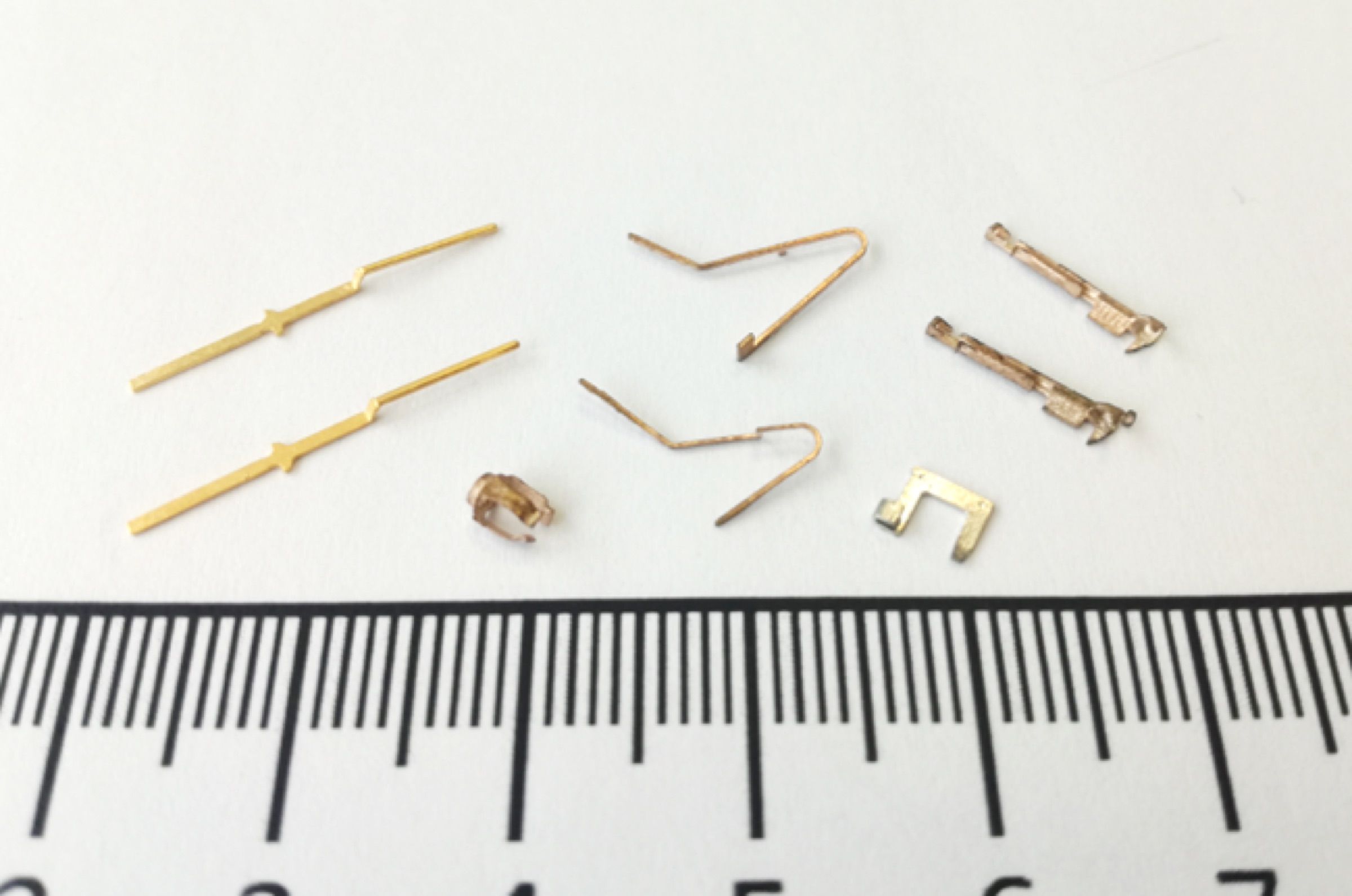 Kleine goldfarbene Prototypteile neben einem Millimetermaßstab